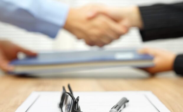 businessman and businesswoman are shaking hands and exchanging folder after agreement was reached