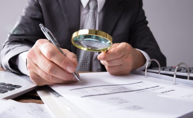 businessperson hand looking at receipts through magnifying glass