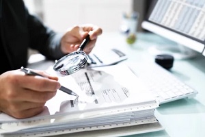 man auditing balance sheet with magnifying glass