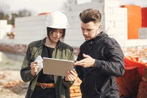 stylish woman architect with tablet and contractor man checking blueprints at construction site