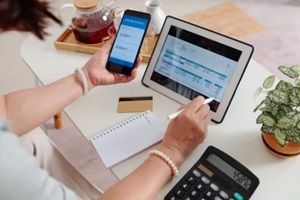 hands of senior woman checking utility bill on screen tablet computer and paying with banking application on smartphone