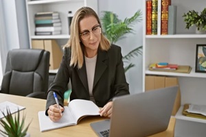 blonde businesswoman, engrossed in work, taking diligent notes at office desk, earphones on