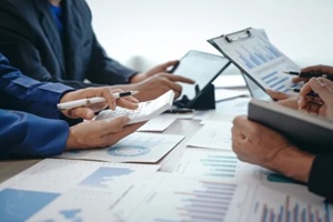 professional business team meeting in formal suits, working at desks with financial papers, calculators, and laptops