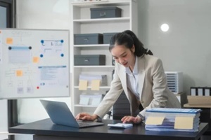 young Asian businesswoman works alone at a desk with a laptop