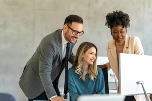 group of happy multiethnic business people in formal wear gathered around computer in office