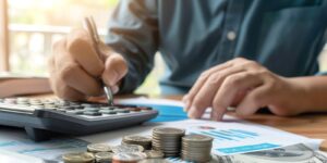 person calculating finances with coins, calculator, and financial documents on desk