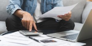 asian young man, male sitting on couch stressed hand calculate expense on table at home
