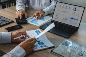 team reviewing accounting financial reports with calculator, charts, tablet, and dashboard on laptop during office meeting