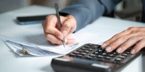 accountant hand using a calculator and writing on financial expense receipt documents at an office desk