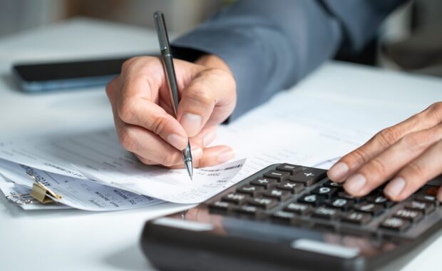 accountant hand using a calculator and writing on financial expense receipt documents at an office desk