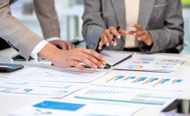 business team reviewing financial charts and reports at a desk during a planning meeting, with laptop, calculator, pens and smartphone